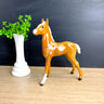 Horse figurine next to a vase with greenery on a wooden surface with a blackboard background